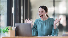 Overjoyed Surprised Woman Looking At Laptop Screen, Sitting At A Work Desk, Reading Good Unexpected News In Email, Message, Excited By Money Refund, Job Promotion, Or Great Sale Offer.