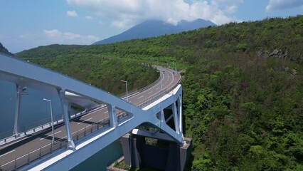 Wall Mural - Kagoshima, Japan: Aerial drone footage traffic on the Ushineo Bridge leading to the Sakurajima volcano in Kagoshima prefecture in the Kyushu island in Japan. Shot with a forward motion