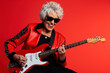 © wolfhound911 - Portrait of a cool trendy old woman playing a guitar on red studio background. Generative AI