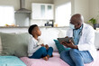 © Wavebreak Media - Senior african american male doctor in face mask using tablet talking to boy patient