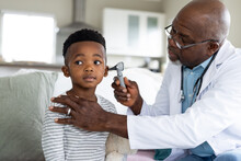 Senior African American Male Doctor Checking Ear Of Boy Patient With Otoscope