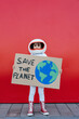 © VISTA by Westend61 - Girl wearing astronaut costume holding Save The Planet placard standing in front of red wall