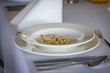 Biały stół ozdobiony białymi talerzami, serwetkami i kieliszkami do wina, ze sztućcami, ustawiony na imprezy
