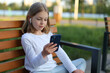 © Andrii Zastrozhnov - A girl child in wireless headphones sits on a bench and looks at the phone.