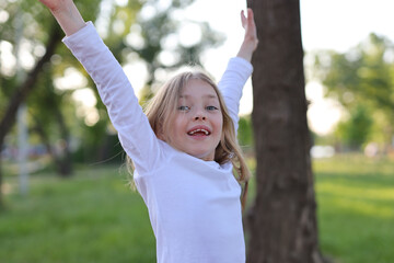 Wall Mural - Rest in the park, happy girl with raised hands on the background of grass and trees.