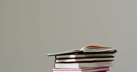 Sticker - Close up of open book on stack of books on grey background, in slow motion