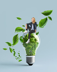  Idea of renewable energy and energy saving. Happy woman is sitting on a light bulb filled with leaves.