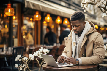 Hipster black man working on his laptop computer in the street cafe