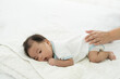 © amorn - Newborn baby sleeping in prone position on bed. Newborn baby or infant lying on white bed while mother’s hands takes care carefully. Family, love and new life concept