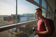 © Chalabala - Smiling man travel by airplane. Passenger looking through window at airport runway while holding wallet with boarding pass in his hand..