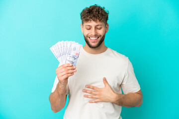 Canvas Print - Young caucasian man taking a lot of money isolated on blue background smiling a lot