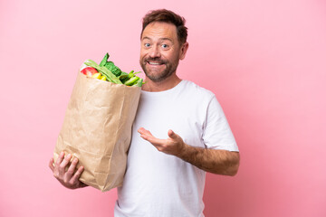 Wall Mural - Middle age man holding a grocery shopping bag isolated on pink background extending hands to the side for inviting to come