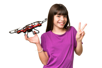 Wall Mural - Little caucasian girl holding a drone over isolated background smiling and showing victory sign