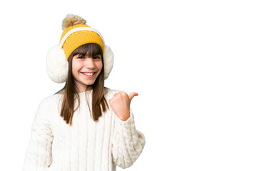 Little caucasian girl wearing winter muffs over isolated background pointing to the side to present a product