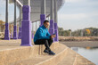 © jroballo - Young latino man in sportswear looks at his mobile phone sitting on some stairs in a public park with copy space.