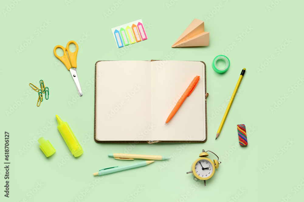 Composition with blank notebook and stationery supplies on green background