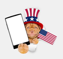 Poster - Happy Mastiff puppy wearing like Uncle Sam looking through a hole in paper and showing big smartphone with white blank screen. isolated on white background