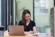 © Songsak C - A beautiful young Asian businesswoman is saving and checking work and documents with her laptop computer at her desk with a bright smile on her face.