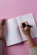 Hands of caucasian woman holding pen and writing in notebook with copy space on pink background