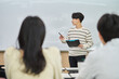 © TEAM PRE-LIGHT - An Asian young man is standing in front of a lecture hall at a university in South Korea, giving a presentation or lecture. In front of him are male and female students.