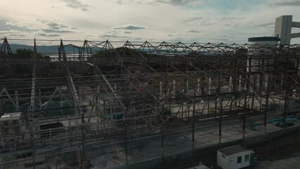 Sticker - Aerial view of an abandoned industrial structure with cranes near a river with sunset cloudy sky