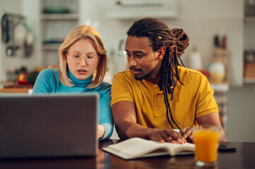 A serious multiracial couple is sitting at home with their laptop and doing calculations for bills and taxes.