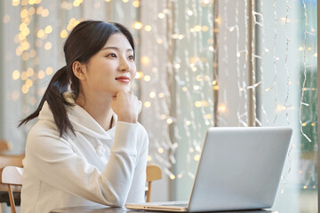 Young female college student model sitting at a cafe table in Asian Korea, listening to a lecture, doing homework or working on a laptop with twinkling lights in the background