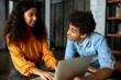 © Anatoliy Karlyuk - Indoor image of happy african american co-workers talking, flirting looking at each other smiling while girl working on laptop, guy with afro hair in denim shirt joking, making her laugh