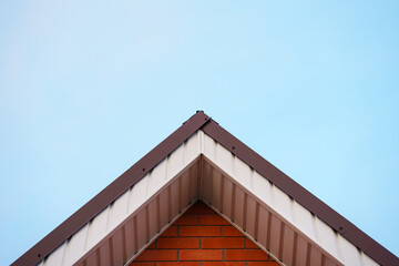 The top of the triangular roof of the house against the sky