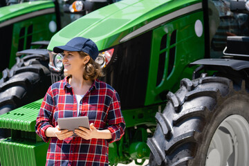 Sticker - Woman farmer with a digital tablet on the background of an agricultural tractor.