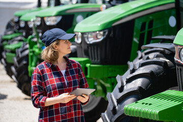 Sticker - Woman farmer with a digital tablet on the background of an agricultural tractors