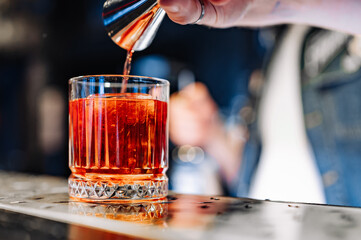 Wall Mural - man bartender hand making negroni cocktail. Negroni classic cocktail and gin short drink with sweet vermouth, red bitter liqueur