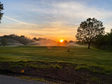 Sprinklers illuminate a golf course at sunrise