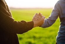 Two Farmers Shake Hands After A Fraction In A Green Wheat Field. Farm Agreement. Negotiation. Agriculture Concept.