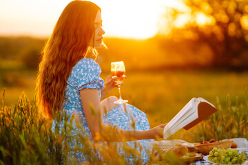 Beautiful woman in a stylish summer dress is resting in the park. A young woman is enjoying the sunset at a picnic. Healthy food. Fashion, nature concept.