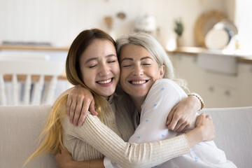 Wall Mural - Positive loving teen girl hugging mature grandma with closed eyes and face touches, sitting on home sofa, enjoying family meeting, leisure, congratulating on mothers day