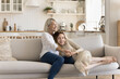© fizkes - Happy pretty grandma hugging cheerful teen granddaughter kid on home sofa, holding hand with love, care, affection, smiling, laughing, speaking, giving comfort, support