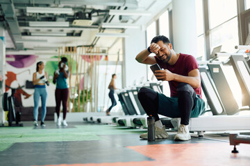 Happy athlete using smart phone while taking break after exercising in gym.