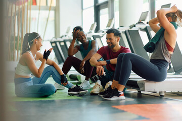 Wall Mural - Happy athletic friends talking while taking break after sports training in gym.