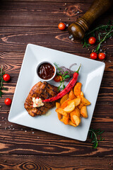 Canvas Print - Fried pork fillet steak with Rustic fried potato wedges, onions, chili peppers, cherry tomatoes and sauce.