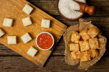 Raw and fried tapioca cubes (Dadinhos de Tapioca) on top of rustic wooden table, top view, selective focus, typical northeastern Brazilian food