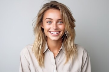 Wall Mural - Portrait of a beautiful young blond woman smiling and looking at camera over grey background