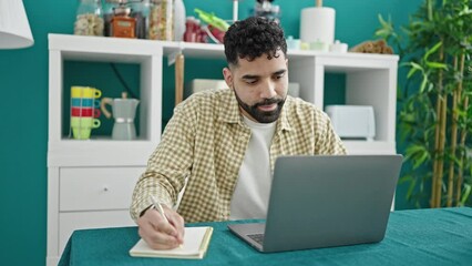 Sticker - Young hispanic man using laptop writing notes at dinning room