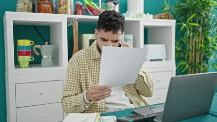 Sticker - Young hispanic man reading document talking on smartphone at dinning room