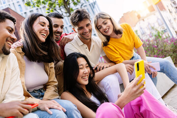 Young group of gen z people having fun using cell phone together outside. Cheerful community of student zoomers enjoying social media content on smartphone app.