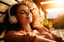 Pretty young woman laying down and relaxing while listening to music on headphones with a smile on her face.