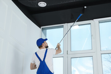 Canvas Print - Worker in uniform painting ceiling with roller indoors