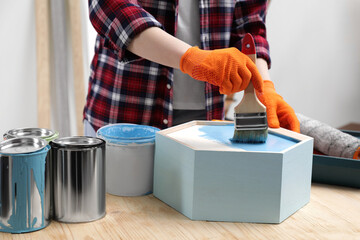 Poster - Woman painting honeycomb shaped shelf with brush at wooden table indoors, closeup