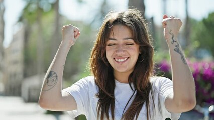 Wall Mural - Young beautiful hispanic woman smiling confident looking to the sky with winner gesture at street