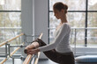 female ballet dancer stretching legs with barre in choreography studio